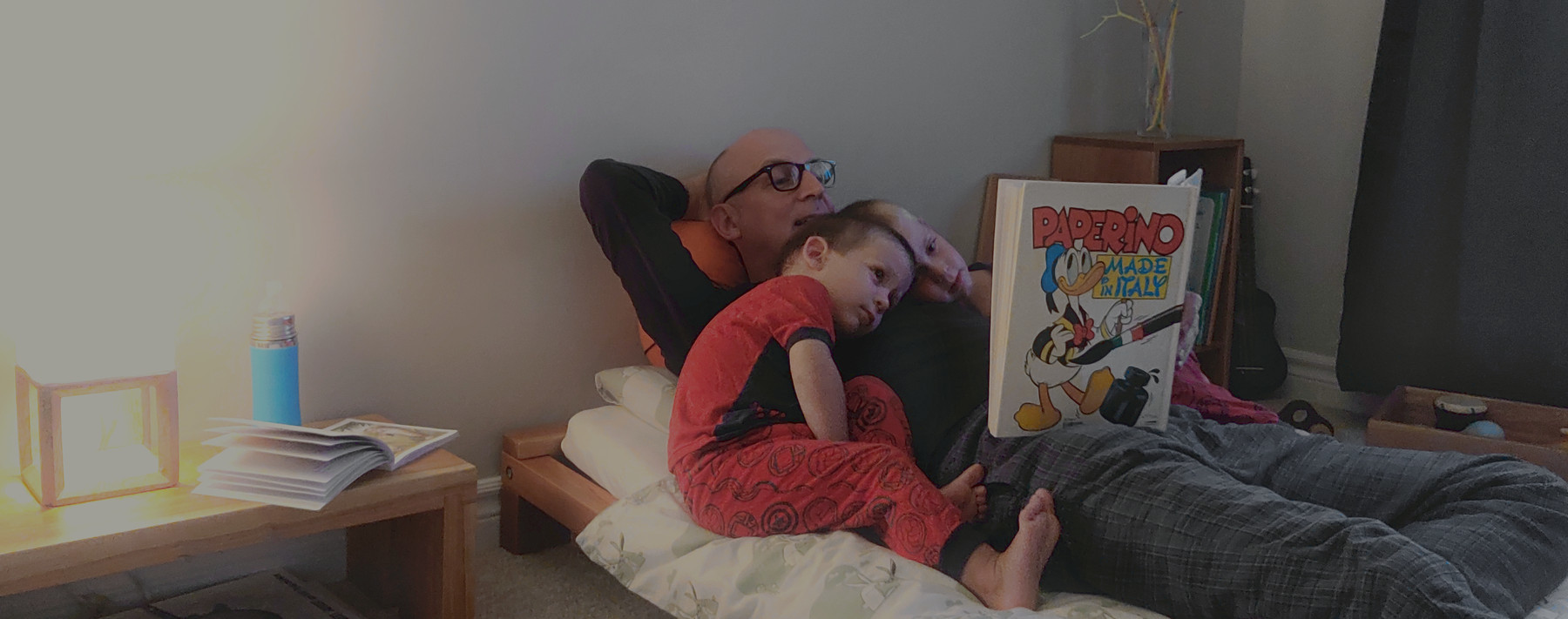 Un père et deux enfants allongés dans un lit Montessori, lisant une histoire