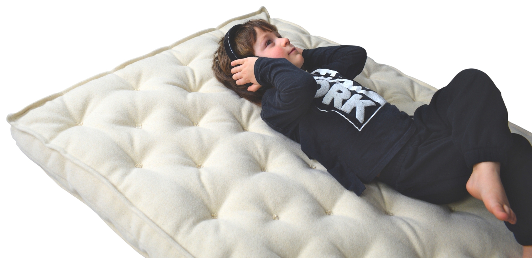 Little boy listening to music laying on a tufted wool mattress